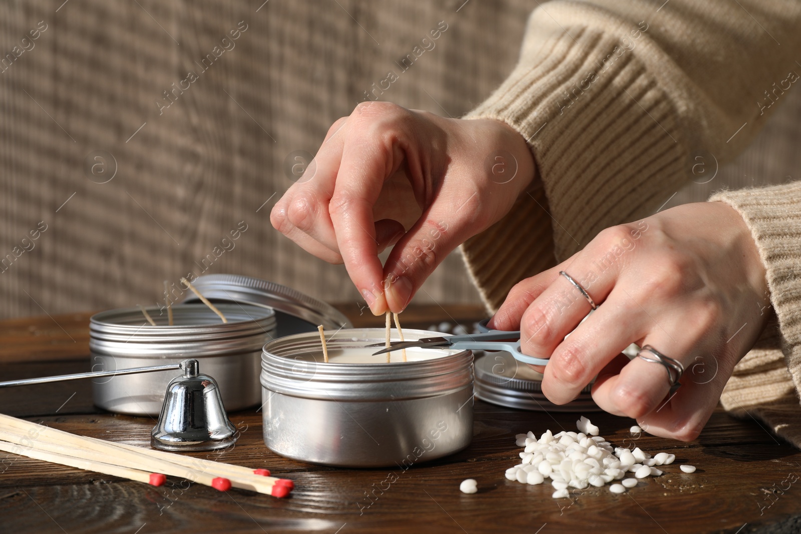 Photo of Woman cutting soy candle wick with scissors at wooden table, closeup