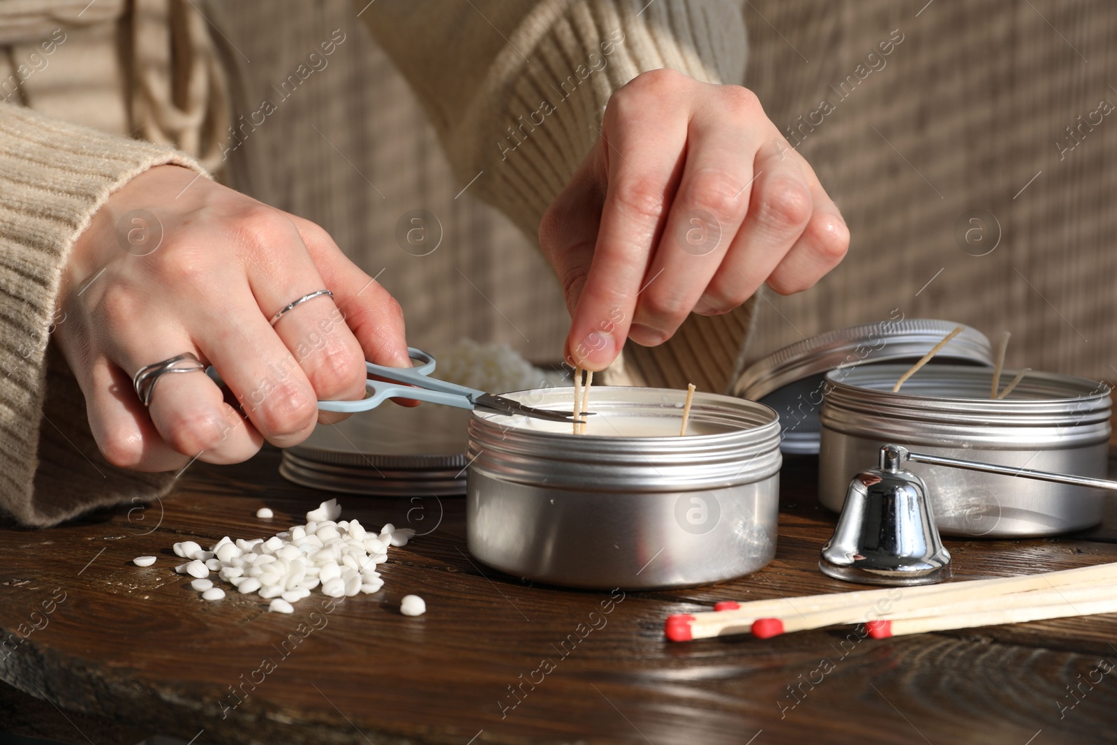 Photo of Woman cutting soy candle wick with scissors at wooden table, closeup