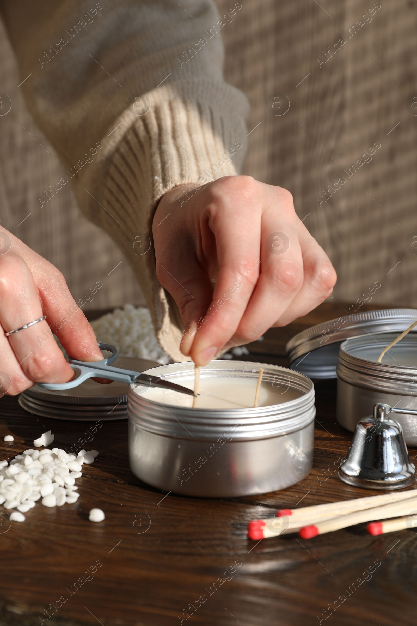 Photo of Woman cutting soy candle wick with scissors at wooden table, closeup