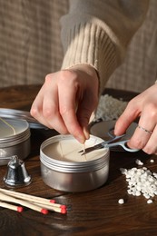 Photo of Woman cutting soy candle wick with scissors at wooden table, closeup