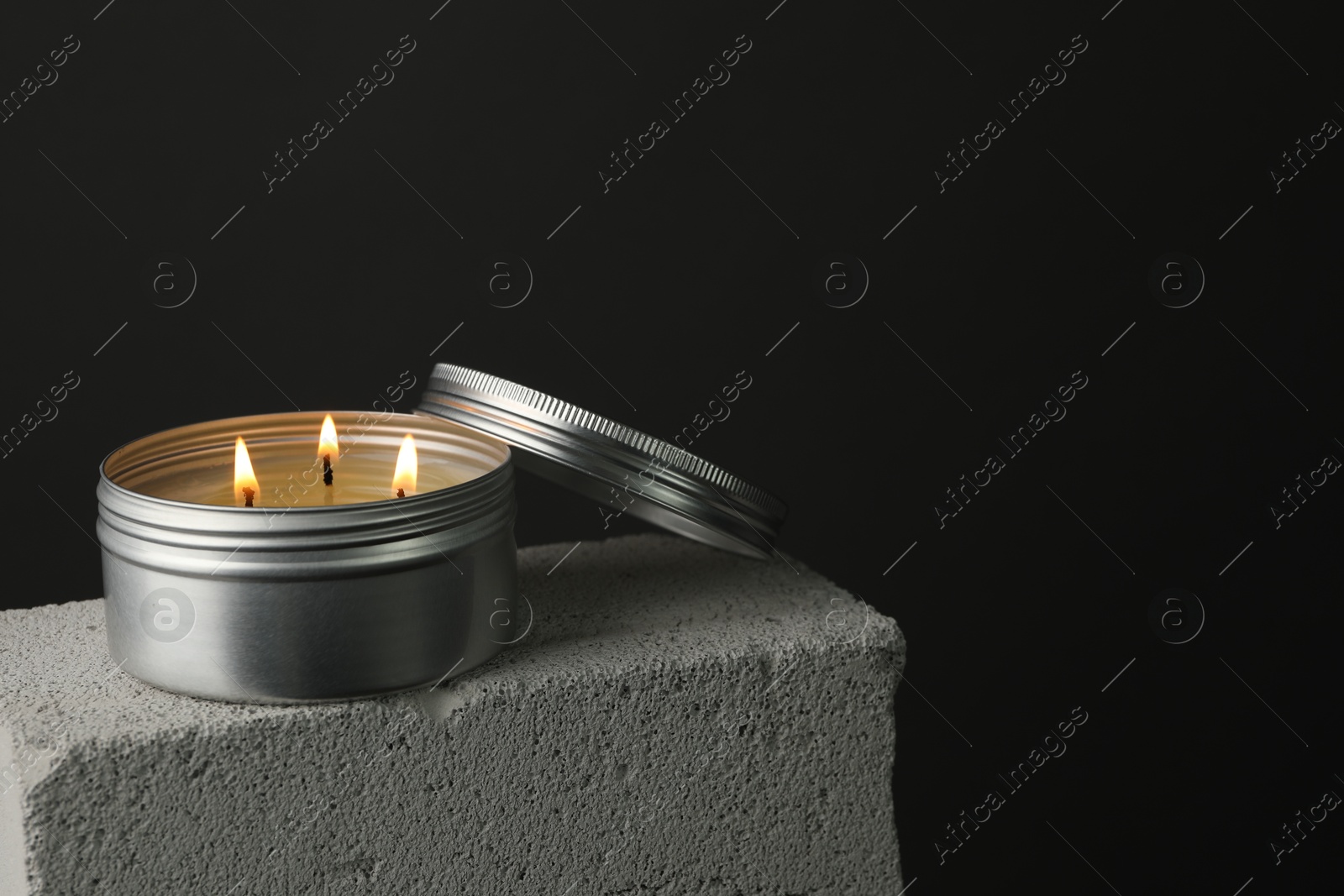 Photo of Burning soy wax candle and lid on concrete block against gray background, space for text