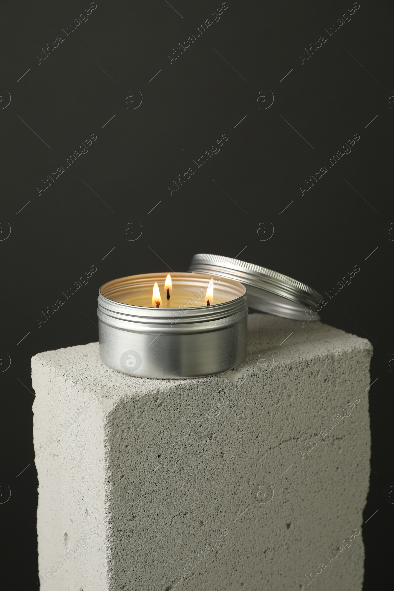 Photo of Burning soy wax candle and lid on concrete block against gray background, space for text