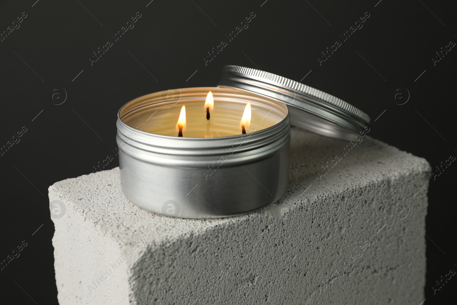 Photo of Burning soy wax candle and lid on concrete block against gray background, closeup