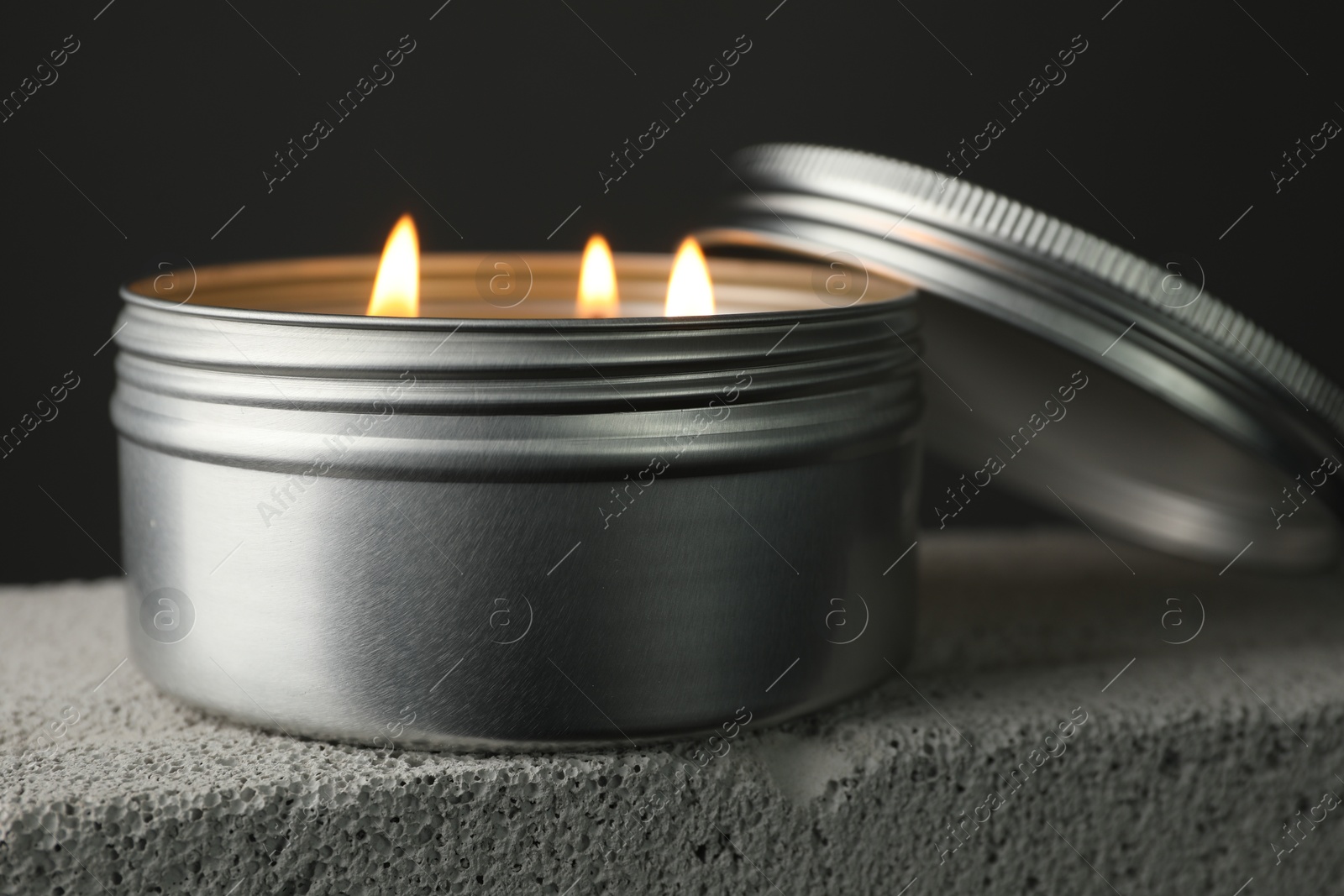 Photo of Burning soy wax candle and lid on concrete block against gray background, closeup