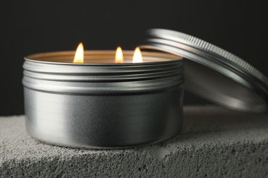 Photo of Burning soy wax candle and lid on concrete block against gray background, closeup