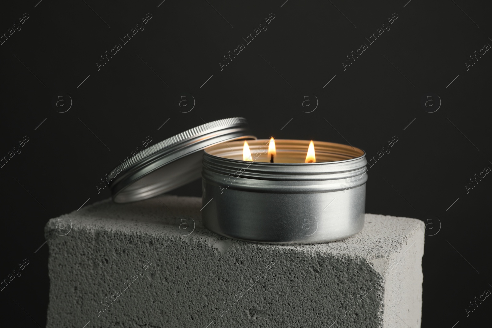 Photo of Burning soy wax candle and lid on concrete block against gray background