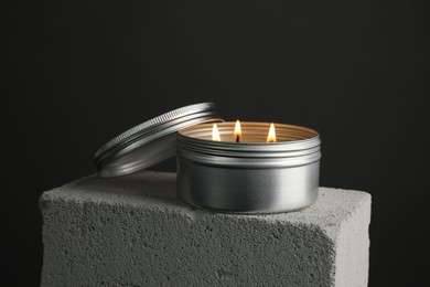 Photo of Burning soy wax candle and lid on concrete block against gray background