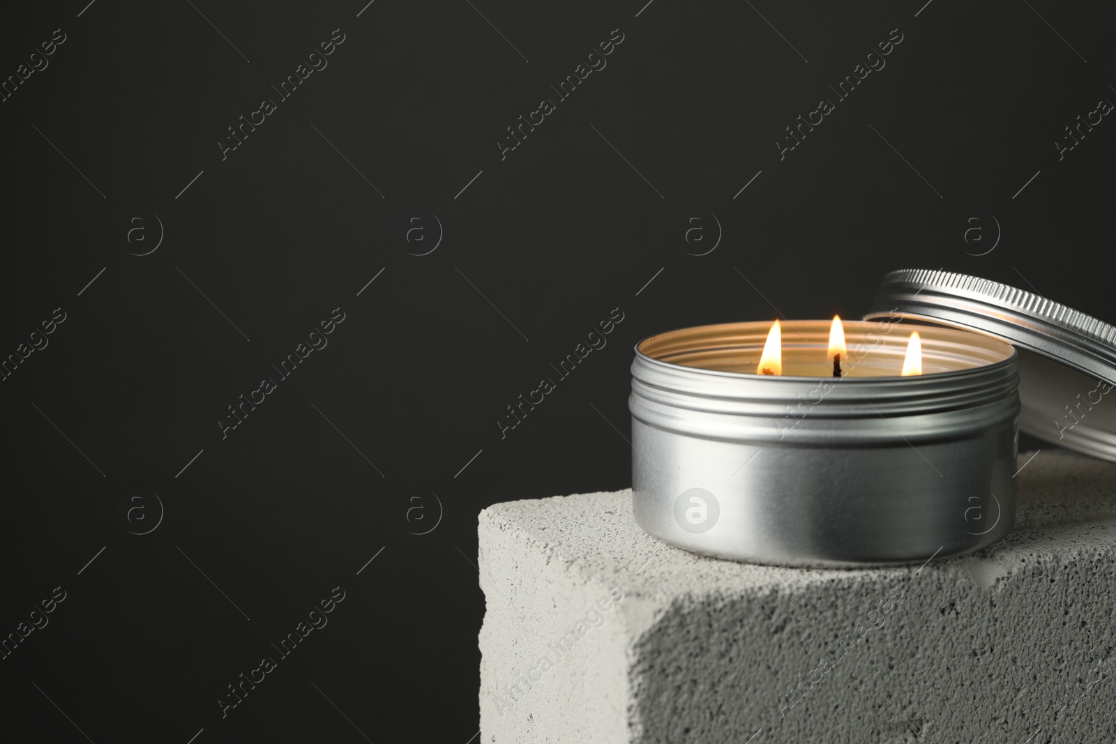 Photo of Burning soy wax candle and lid on concrete block against gray background, space for text