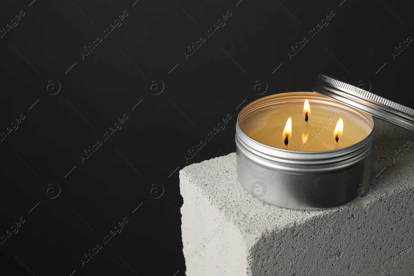 Photo of Burning soy wax candle and lid on concrete block against gray background, space for text