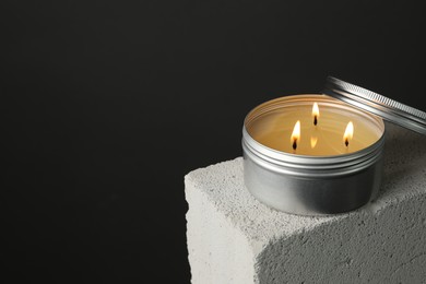 Photo of Burning soy wax candle and lid on concrete block against gray background, space for text