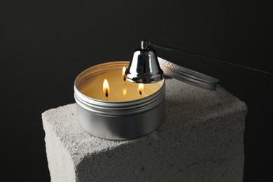 Photo of Extinguishing burning soy wax candle with snuffer on concrete block against gray background, closeup