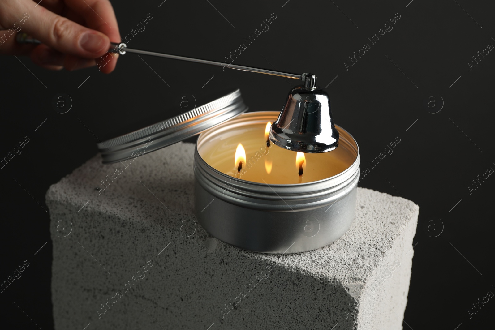 Photo of Woman extinguishing burning soy wax candle with snuffer against gray background, closeup