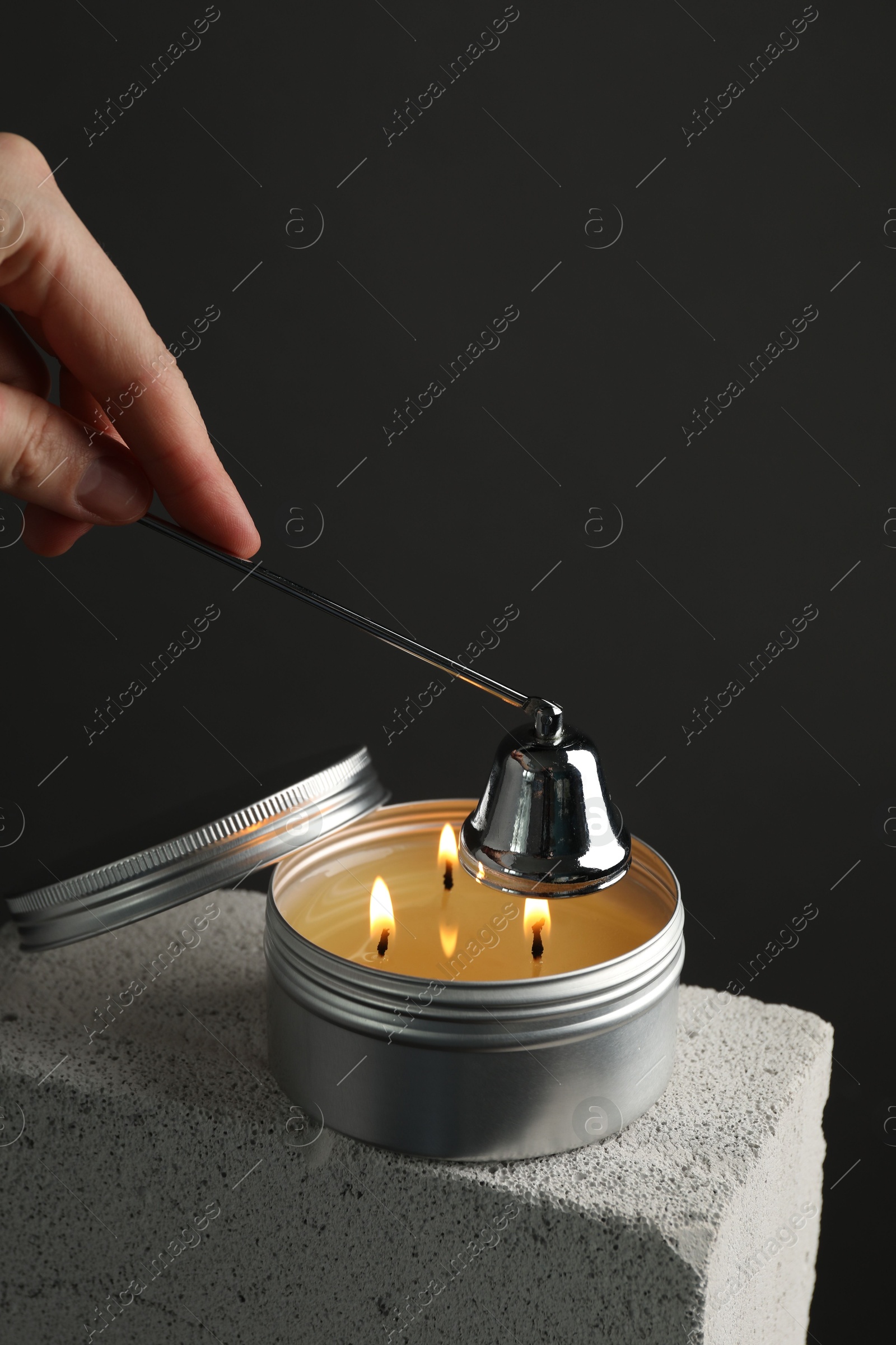 Photo of Woman extinguishing burning soy wax candle with snuffer against gray background, closeup. Space for text