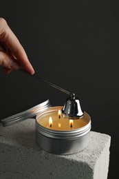 Photo of Woman extinguishing burning soy wax candle with snuffer against gray background, closeup. Space for text