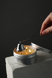 Photo of Woman extinguishing burning soy wax candle with snuffer against gray background, closeup. Space for text