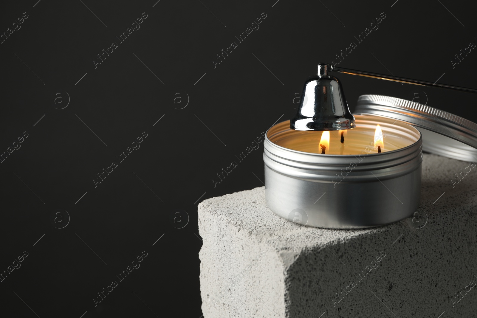 Photo of Extinguishing burning soy wax candle with snuffer on concrete block against gray background, closeup. Space for text