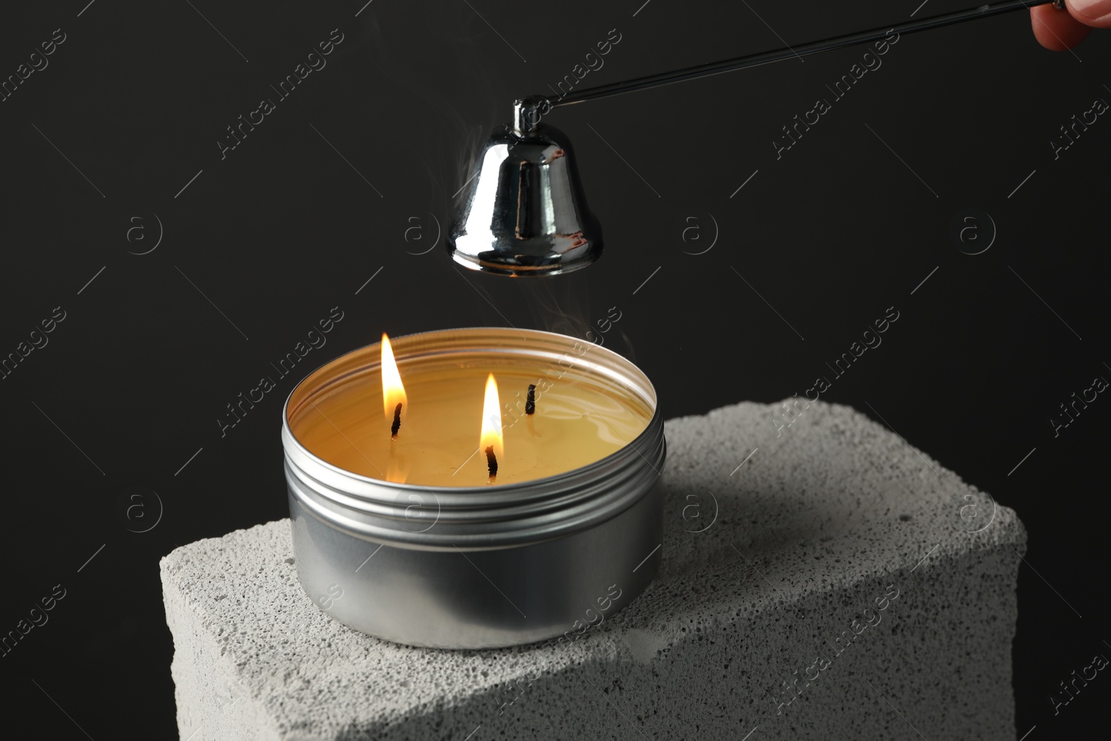 Photo of Extinguishing burning soy wax candle with snuffer on concrete block against gray background, closeup