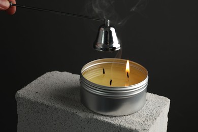 Photo of Extinguishing burning soy wax candle with snuffer on concrete block against gray background, closeup