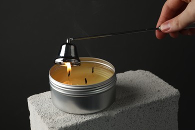 Photo of Woman extinguishing burning soy wax candle with snuffer against gray background, closeup