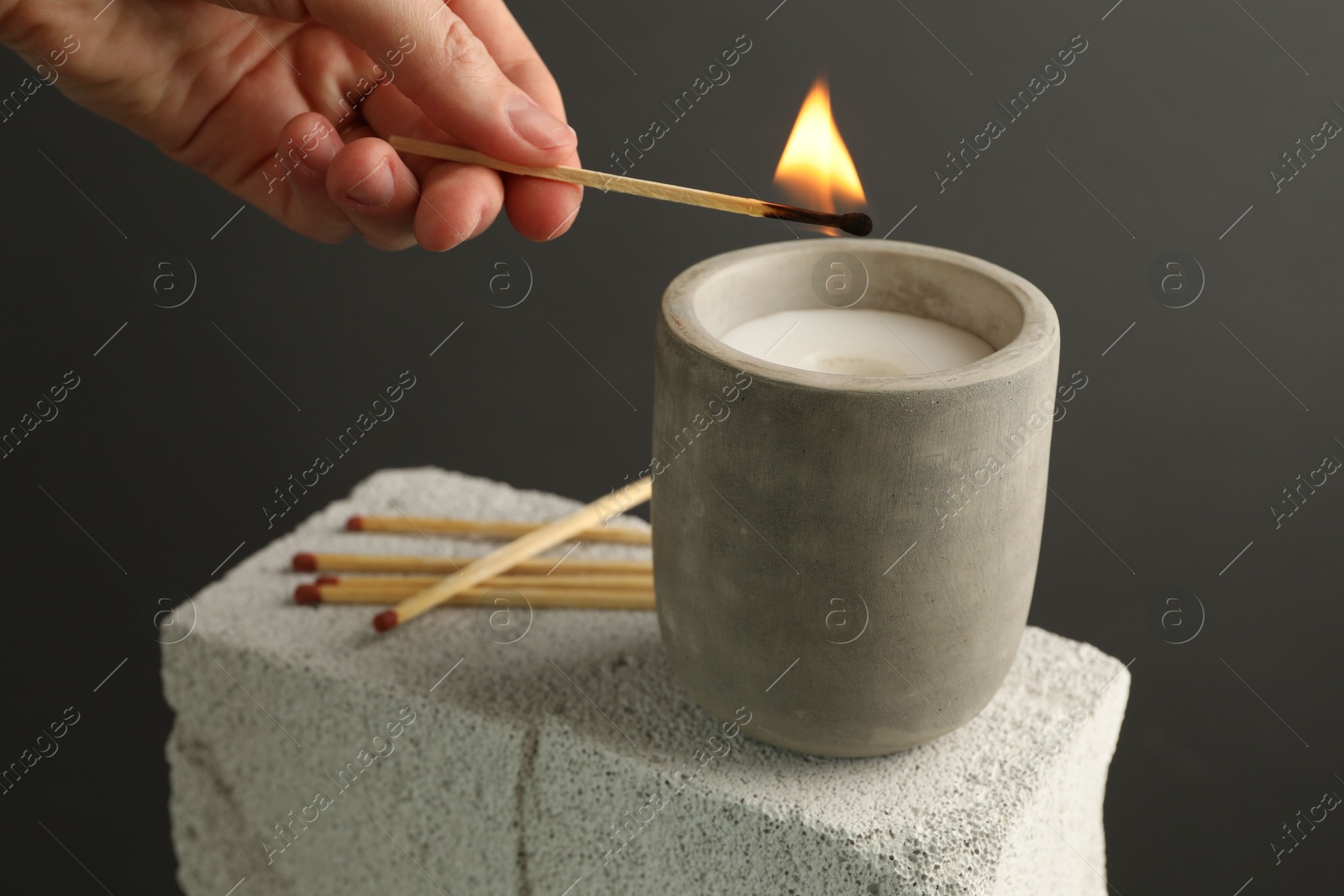 Photo of Woman lighting soy wax candle with long match against gray background, closeup