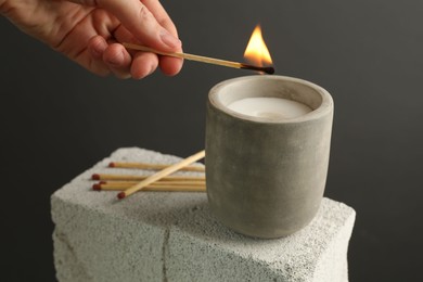 Photo of Woman lighting soy wax candle with long match against gray background, closeup