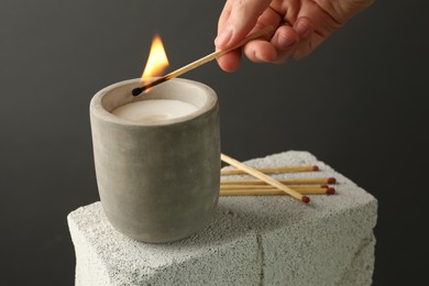 Photo of Woman lighting soy wax candle with long match against gray background, closeup