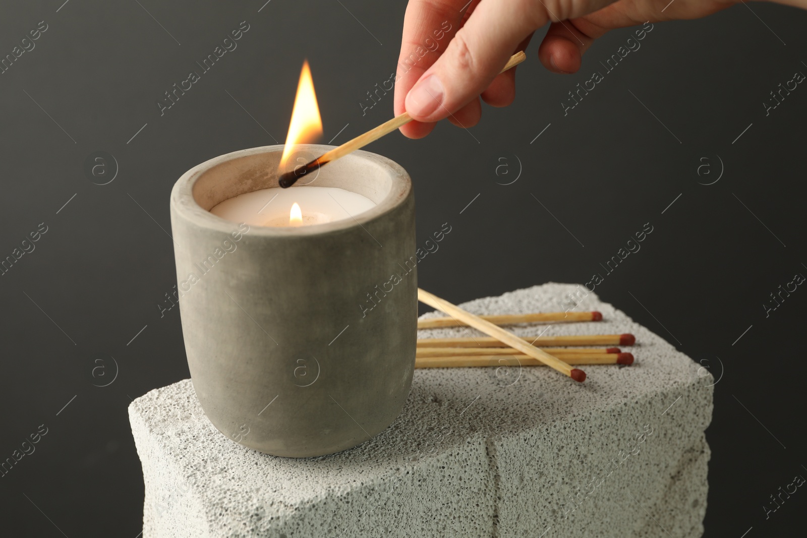 Photo of Woman lighting soy wax candle with long match against gray background, closeup