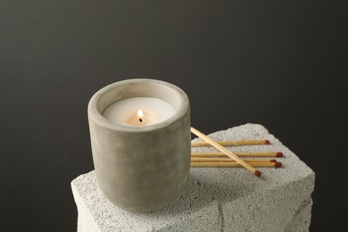 Photo of Burning soy wax candle and matches on concrete block against gray background, space for text