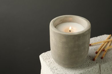 Photo of Burning soy wax candle and matches on concrete block against gray background, space for text