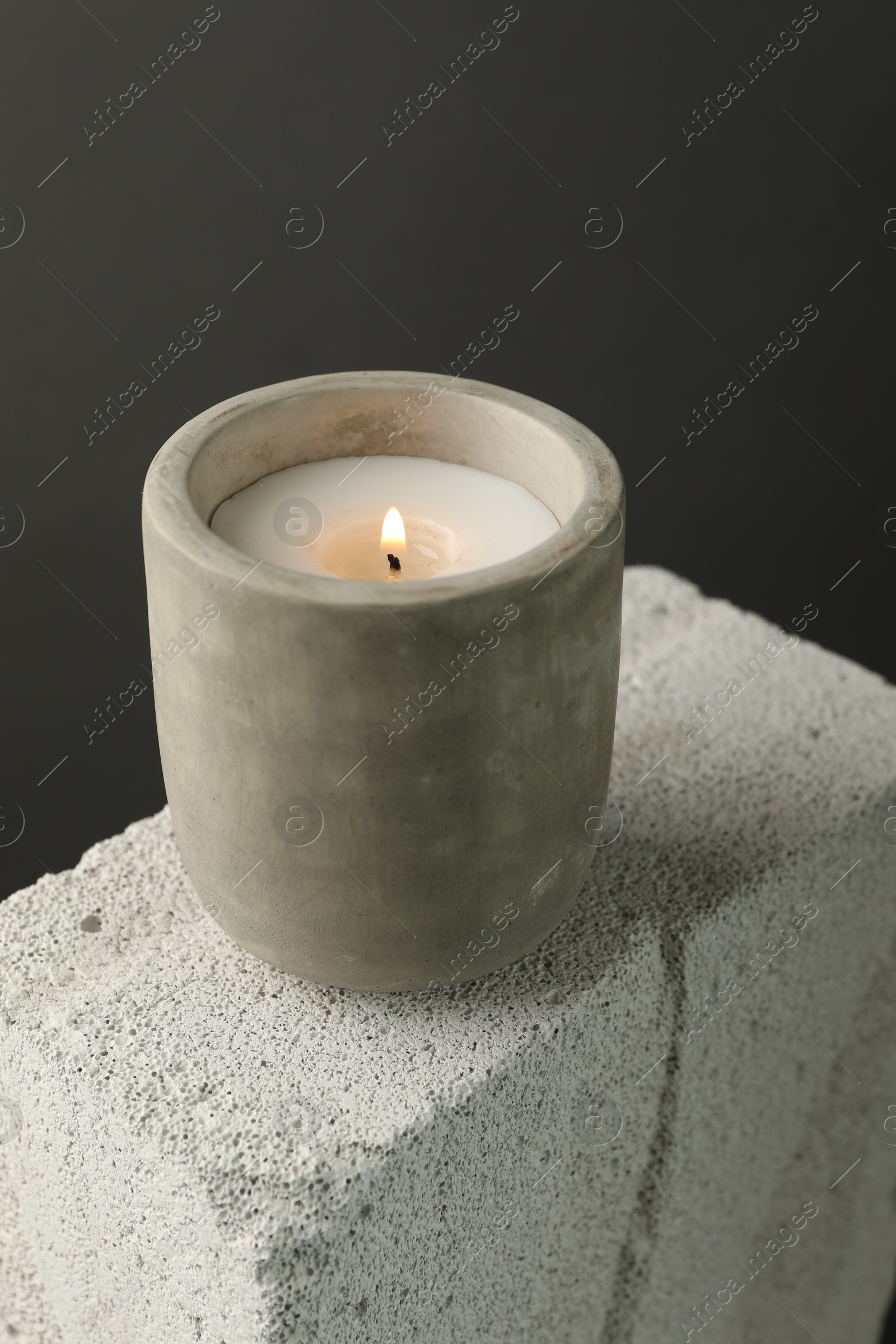 Photo of Burning soy wax candle on concrete block against gray background