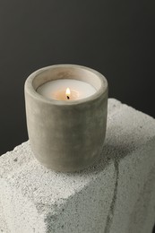 Photo of Burning soy wax candle on concrete block against gray background