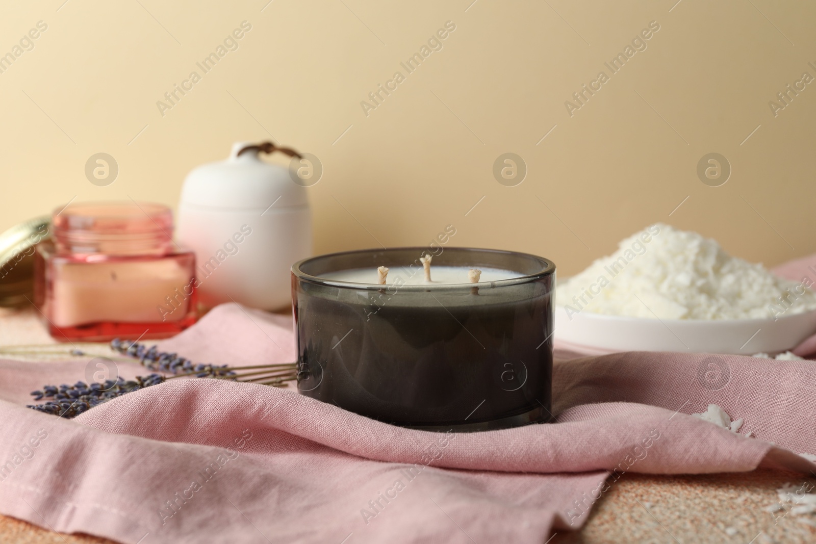 Photo of Soy wax candle, pink napkin and lavender flowers on table against beige background