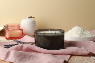 Photo of Soy wax candle, pink napkin and lavender flowers on table against beige background