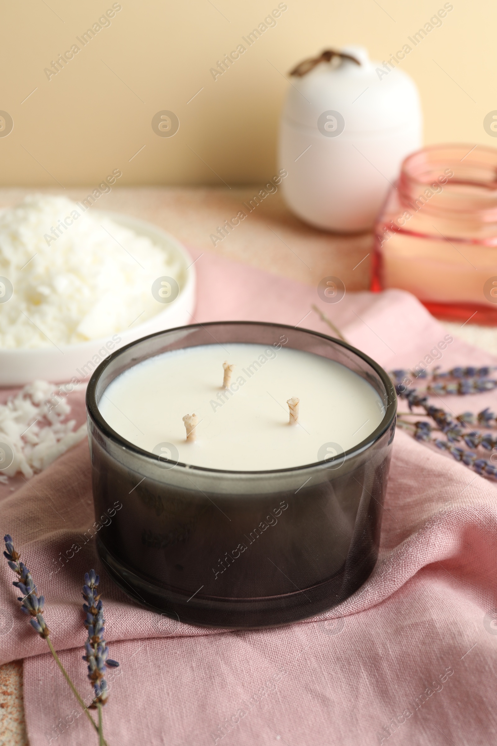 Photo of Soy wax candle, pink napkin and lavender flowers on table against beige background