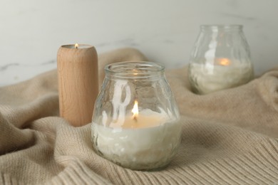 Photo of Burning soy wax candles and beige warm fabric on light table, closeup