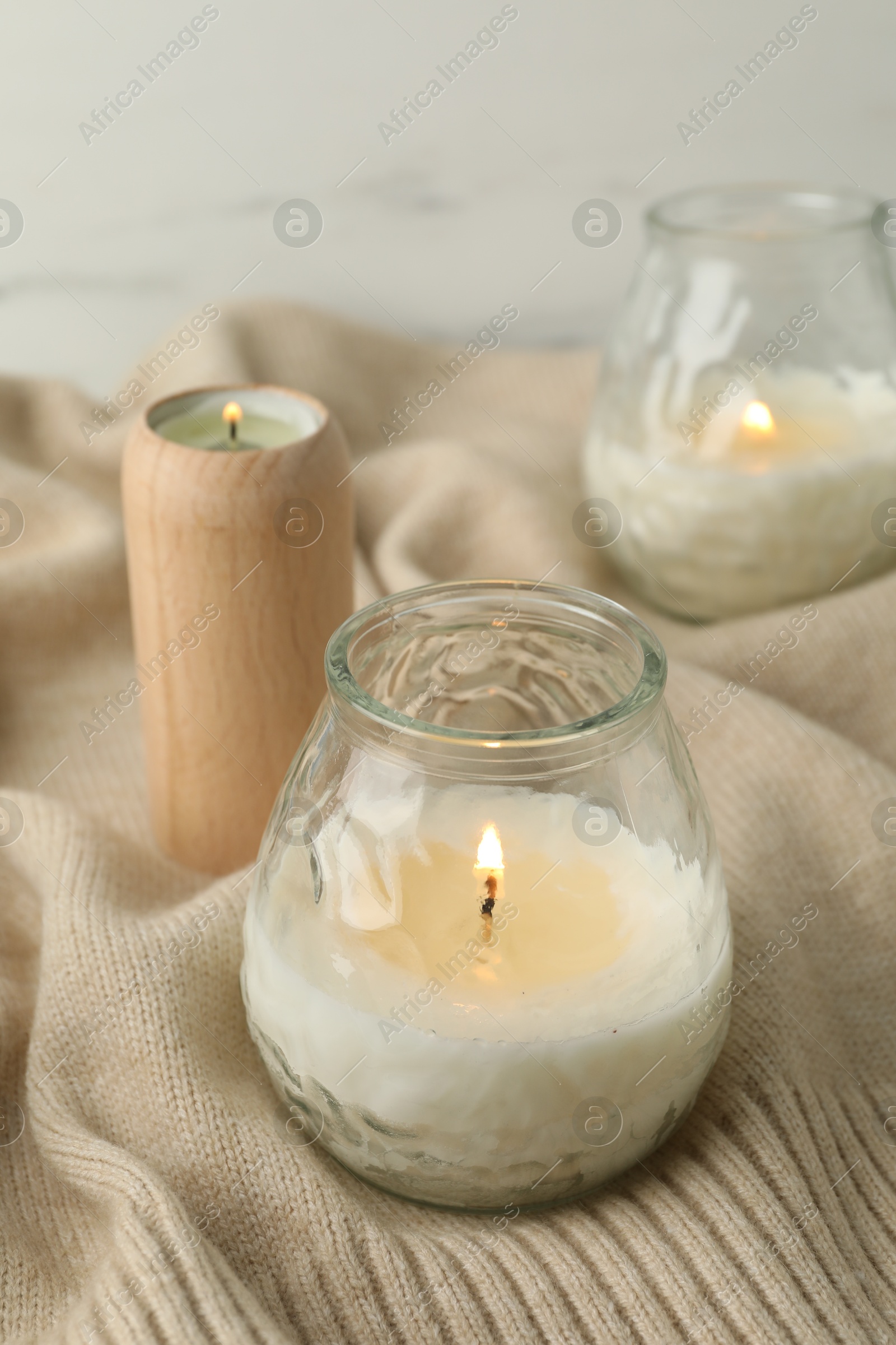 Photo of Burning soy wax candles and beige warm fabric on light table, closeup