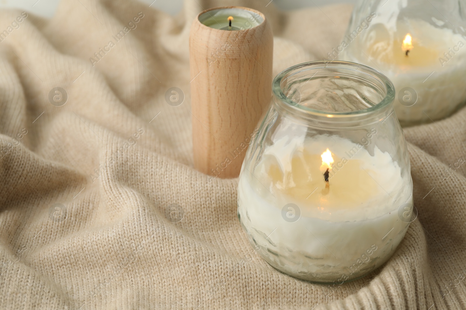 Photo of Burning soy wax candles on beige warm fabric, closeup. Space for text