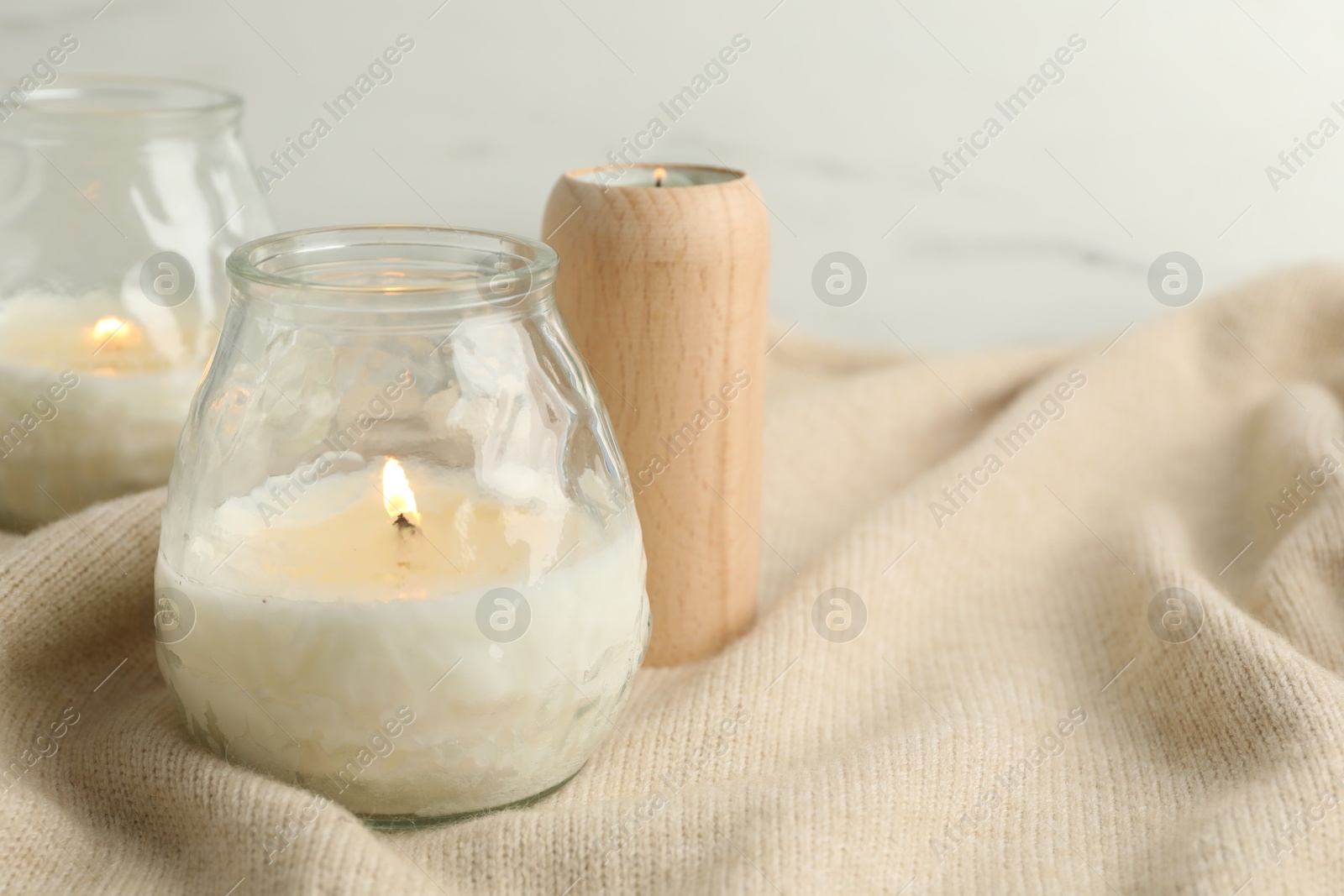 Photo of Burning soy wax candles and beige warm fabric on light table, closeup. Space for text