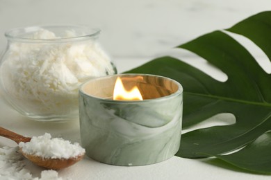 Photo of Burning soy wax candle, monstera leaf and spoon on light table, closeup