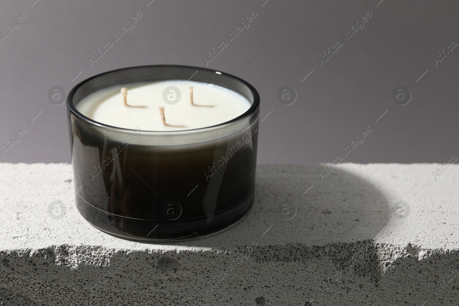 Photo of Soy wax candle on concrete block against gray background, space for text