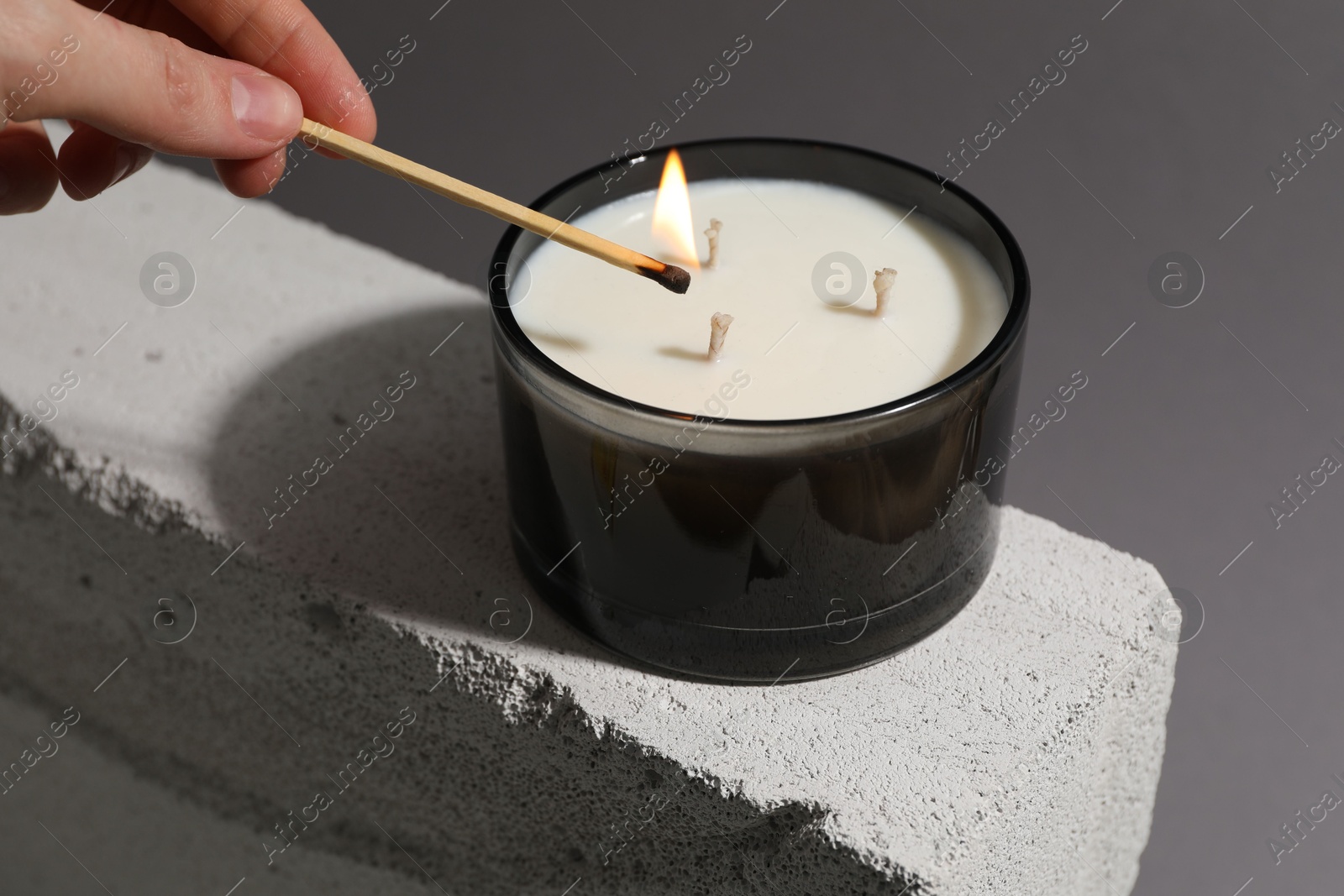 Photo of Woman lighting soy wax candle with long match against gray background, closeup