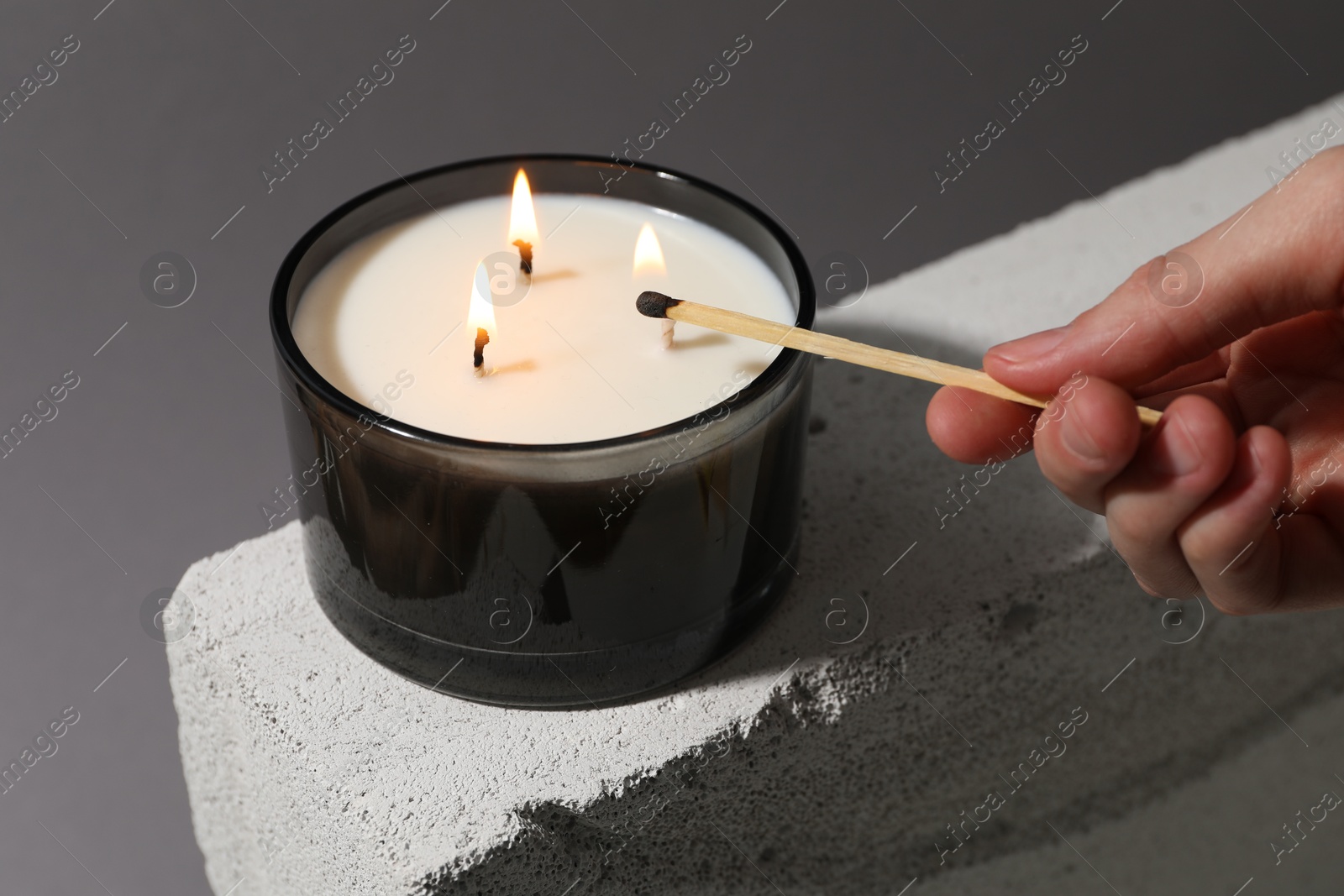 Photo of Woman lighting soy wax candle with long match against gray background, closeup