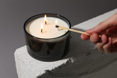 Photo of Woman lighting soy wax candle with long match against gray background, closeup