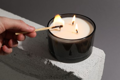 Photo of Woman lighting soy wax candle with long match against gray background, closeup