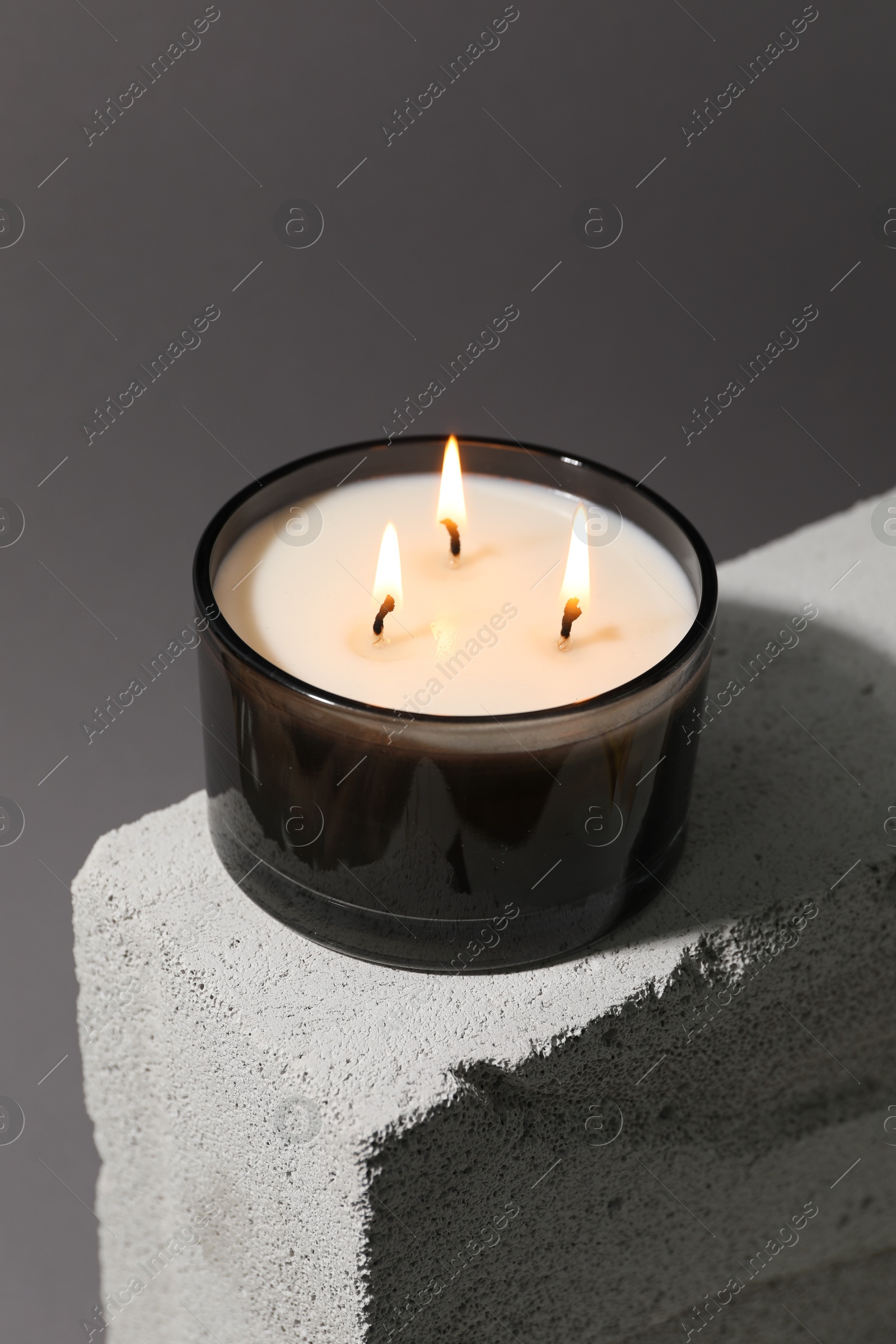 Photo of Burning soy wax candle on concrete block against gray background