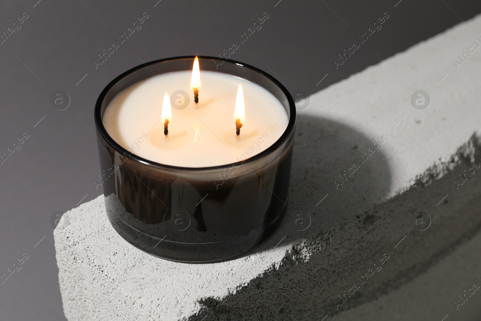 Photo of Burning soy wax candle on concrete block against gray background