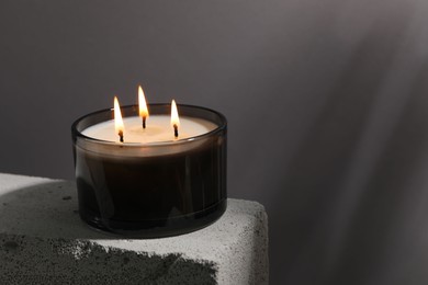 Photo of Burning soy wax candle on concrete block against gray background, space for text