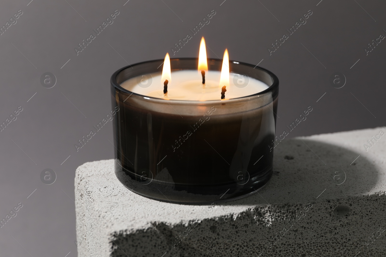 Photo of Burning soy wax candle on concrete block against gray background, closeup