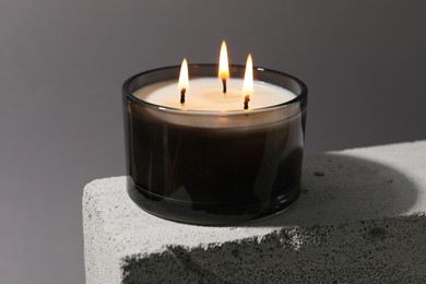 Photo of Burning soy wax candle on concrete block against gray background, closeup