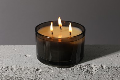 Photo of Burning soy wax candle on concrete block against gray background, closeup